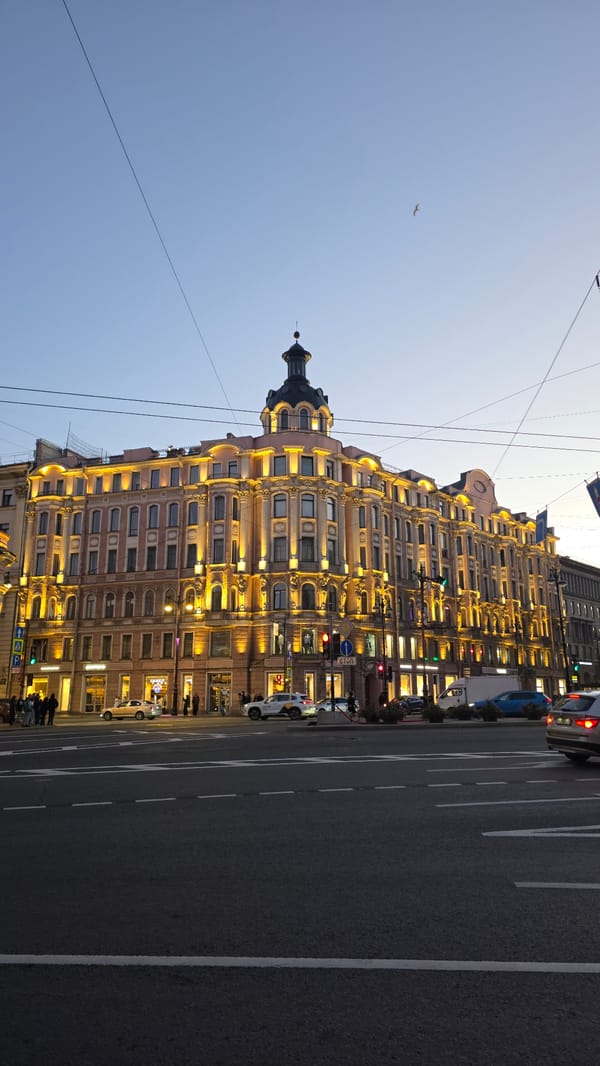 Ornate urban street glows at dusk, buildings lit and sky fading