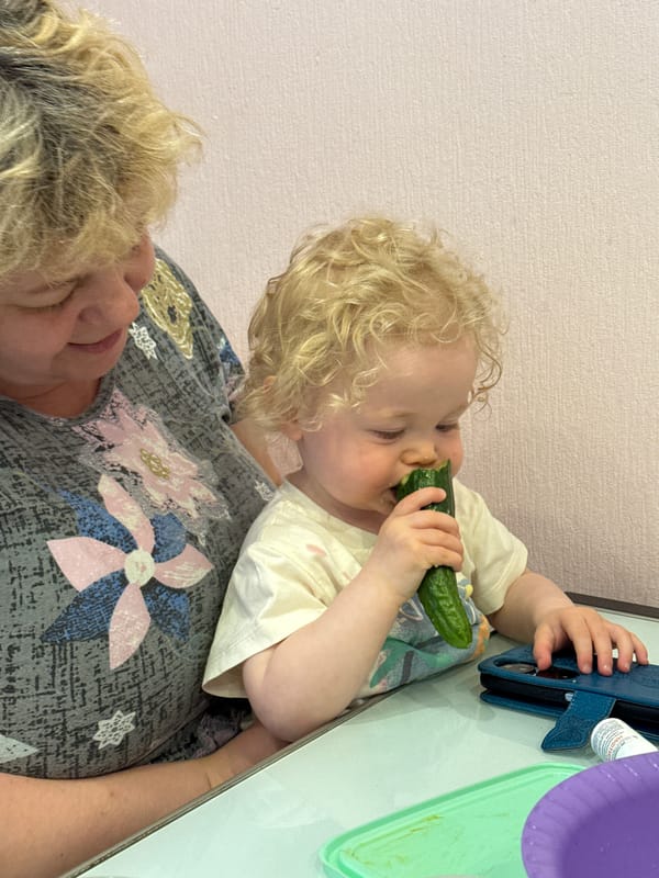 Toddler enjoys cucumber snack with caregiver in Vladimir