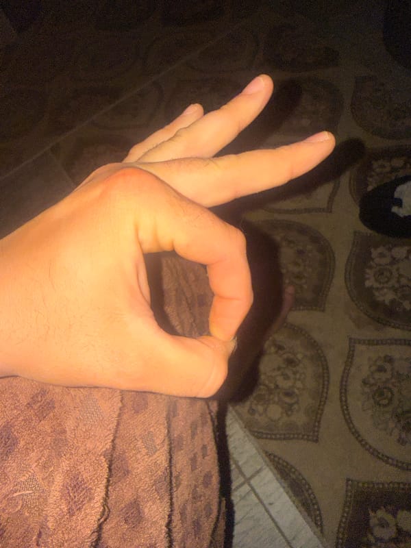 Person Makes OK Hand Gesture Against Patterned Bedding