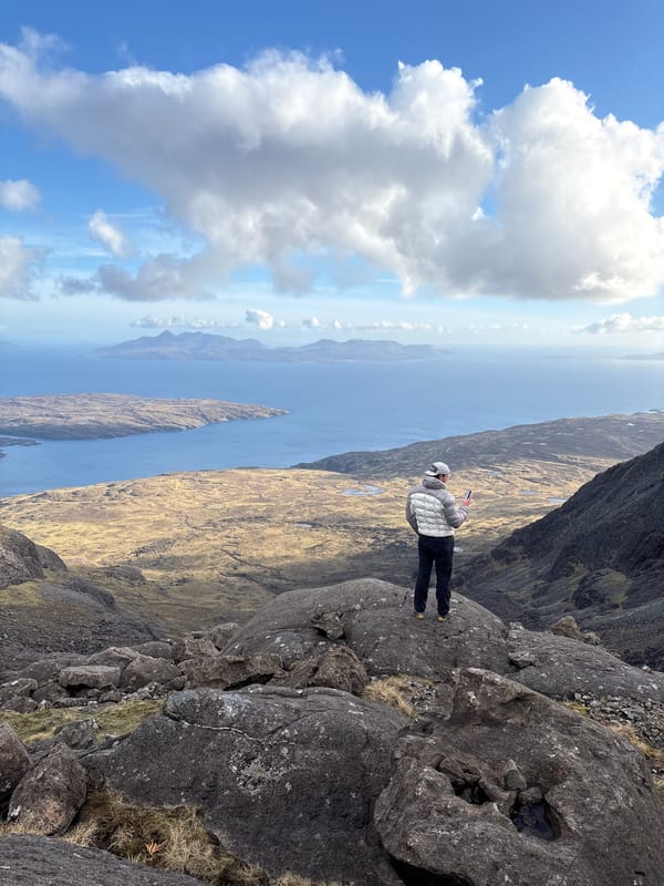 Person stands on rocky outcrop overlooking Scottish coastal landscape