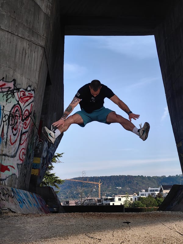Man performs athletic stunts near graffitied concrete structure early morning