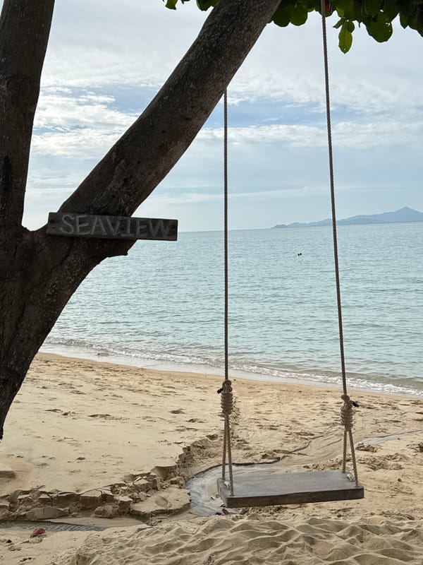Beachside swing and white lighthouse along a sunny waterfront