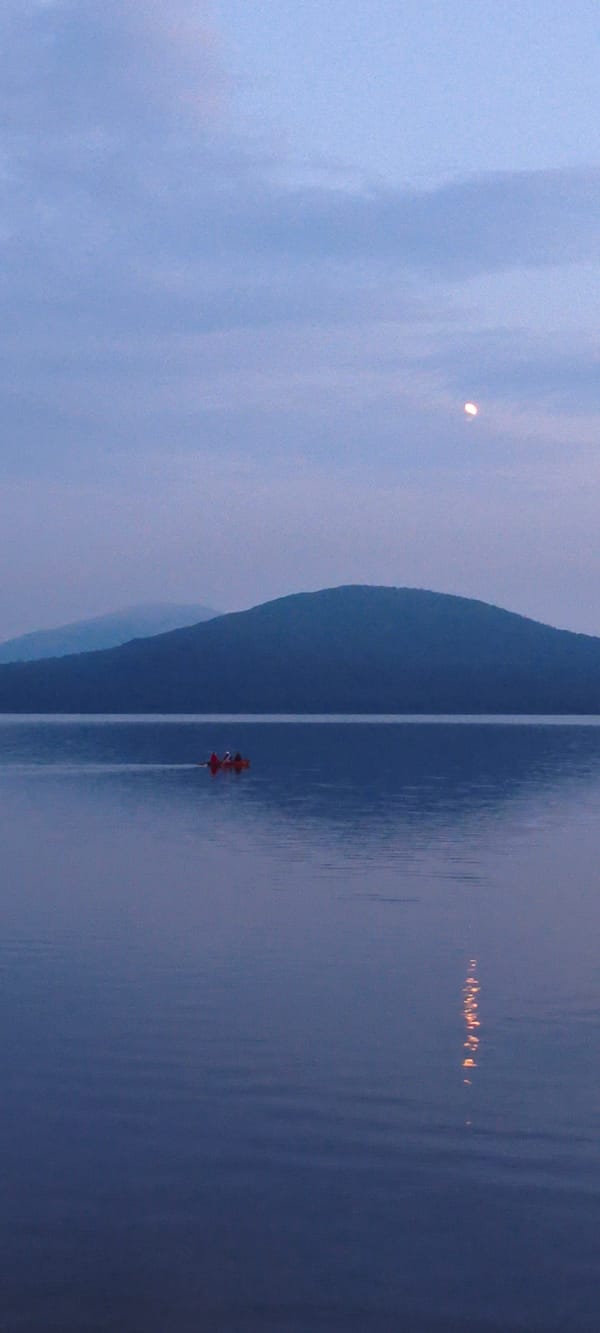 Red canoe crossing calm water at dusk in Zyuratkul'
