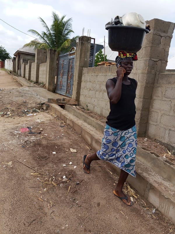 Woman carries household items on dirt road in Nigeria