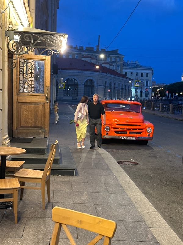 Vintage orange truck parked by a St. Petersburg canal at dusk