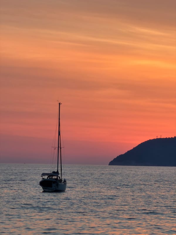 Golden hour on a Bar, Montenegro beach with a sailboat offshore.