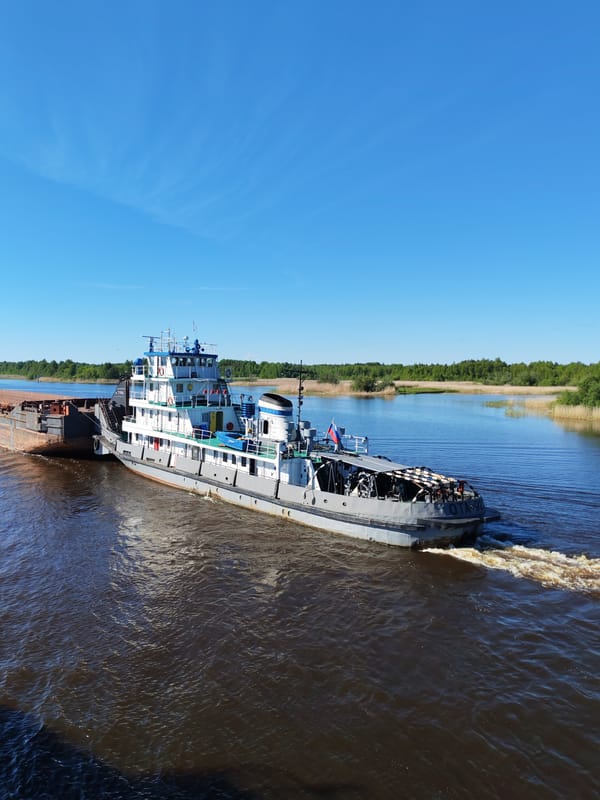 Tugboat pushes cargo barge on Russian river near Kargulino