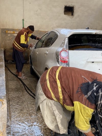 Car wash attendants clean white hatchback in Kandahar