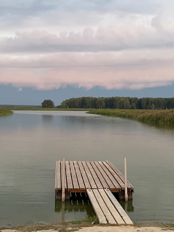Calm water and a wooden pier under cloudy skies in Novopichugovo