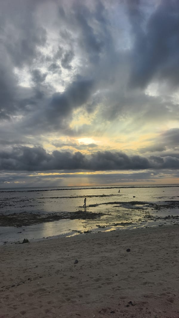 Two people walk on Indonesian beach under cloudy skies