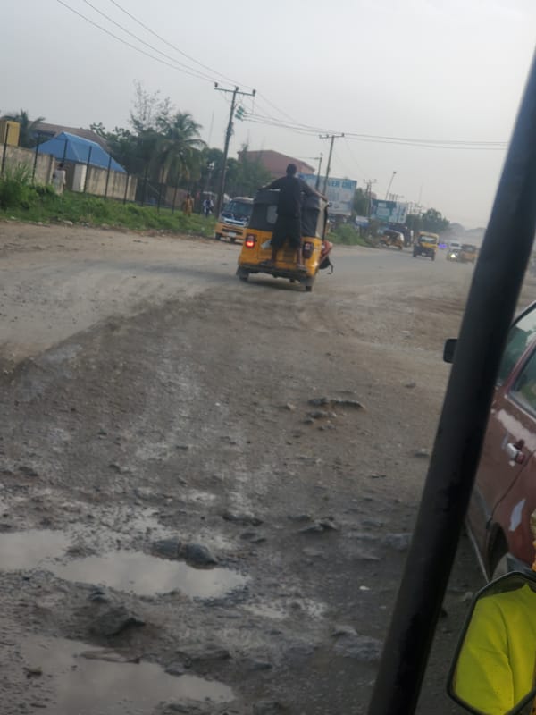 Yellow tricycle navigates pothole-filled unpaved road