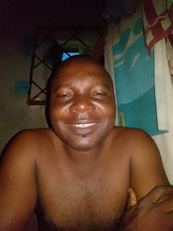 Man photographed smiling by window in Nigerian village