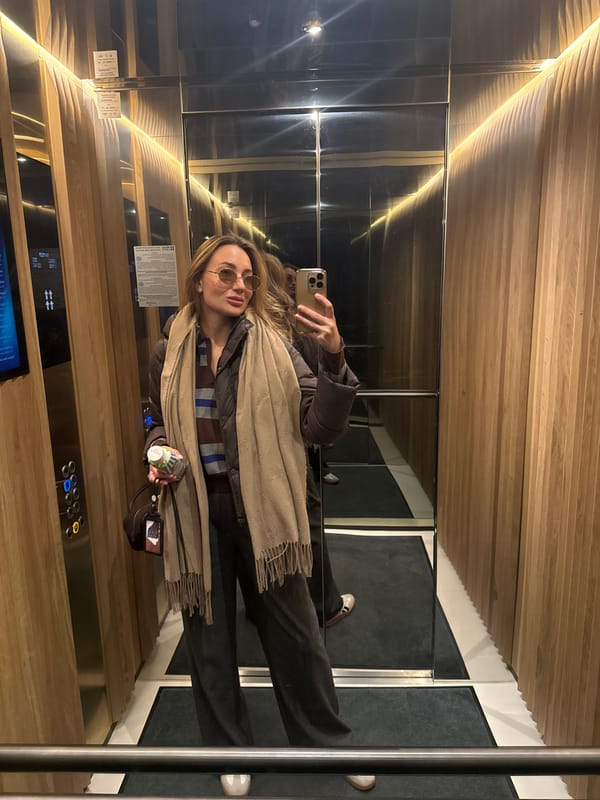 Woman takes selfie in wood-paneled elevator while holding bottle