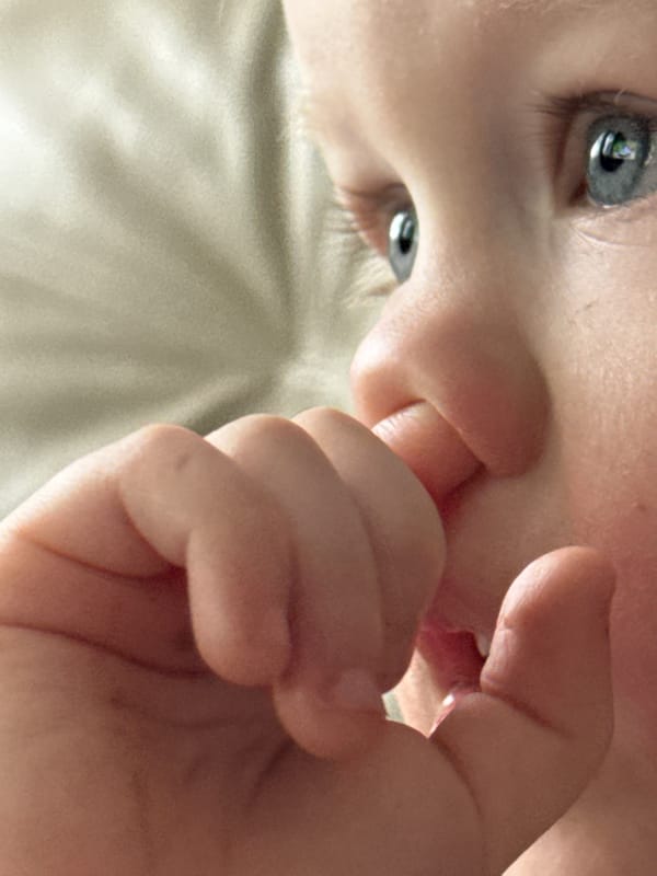 Baby photographed sucking fingers while lying on back