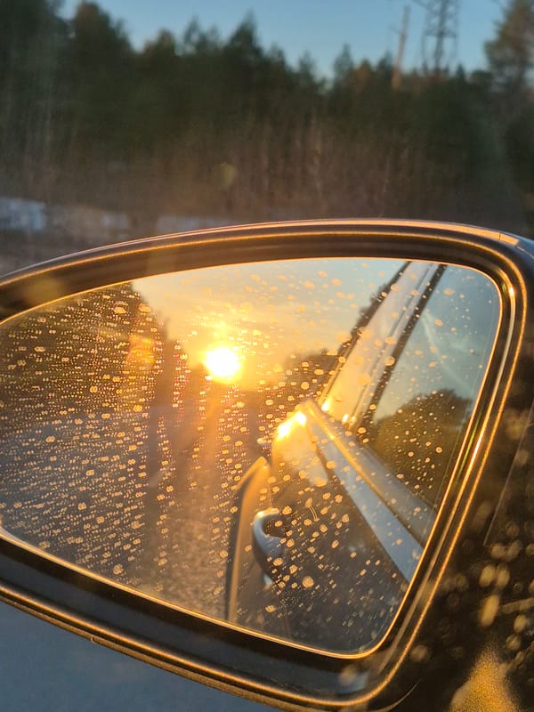 Water-droplet covered car mirror reflects orange sunset in Russia