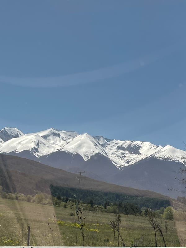 Snow-capped mountains overlook green valley in Dobrinishte, Bulgaria