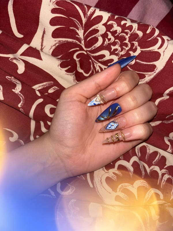 Person showcases elaborate artificial nail art against fabric backdrop
