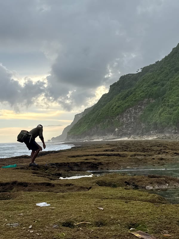 Person observed on rocky shore near clifftop structures in Pecatu