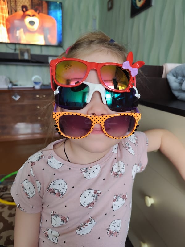 Girl stacks three colorful sunglasses indoors in Russia