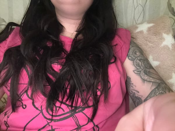 Person relaxing at home with tattoos, pink shirt, laptop
