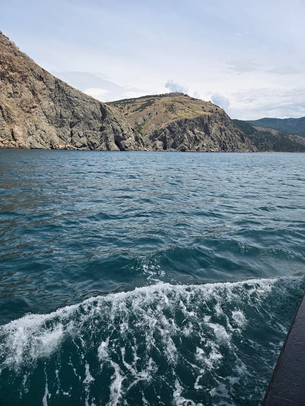 Boat approaches rocky coastline under cloudy skies