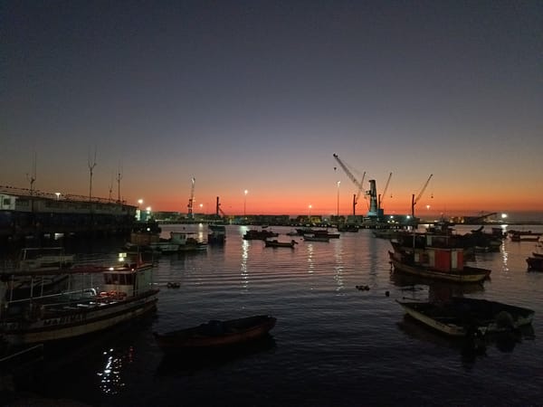Arica harbor at dusk, boats and cranes under a sunset sky