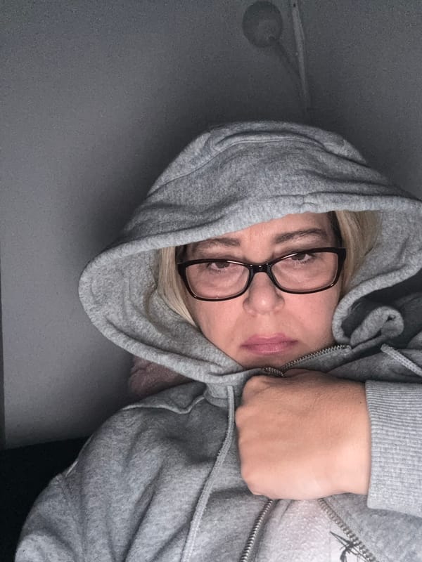 Hooded figure adjusts glasses in dimly lit room