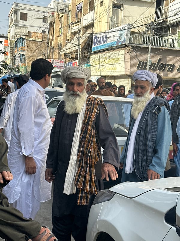 People gather on street near white car in Quetta