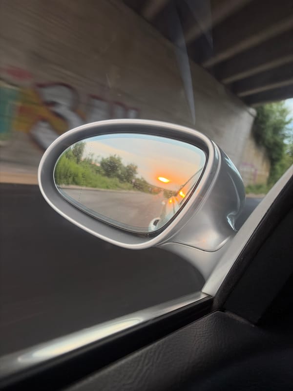 Sunset caught in a rear-view mirror under a graffiti overpass