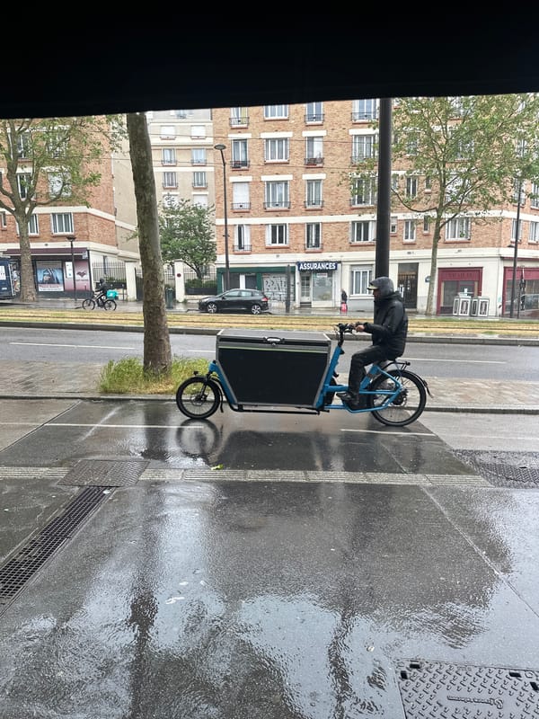 Courier cycles blue cargo bike through wet Paris streets