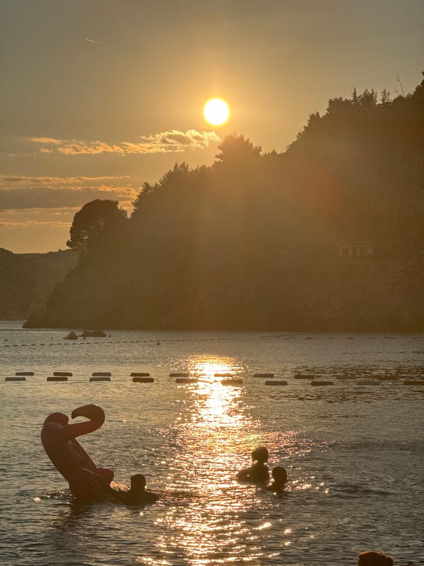 Kamenovo Beach at sunset, crowds, calm water, and an abandoned building nearby