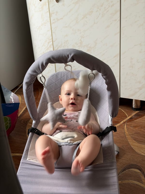 Baby in cat-print onesie relaxes and fusses in grey bouncer