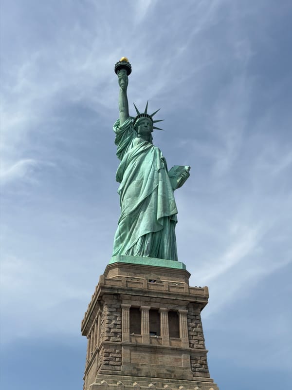 Tourist photographs Statue of Liberty from below against cloudy sky