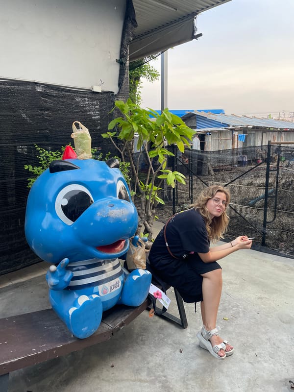 Woman poses with blue cartoon statue in Bangkok street scene