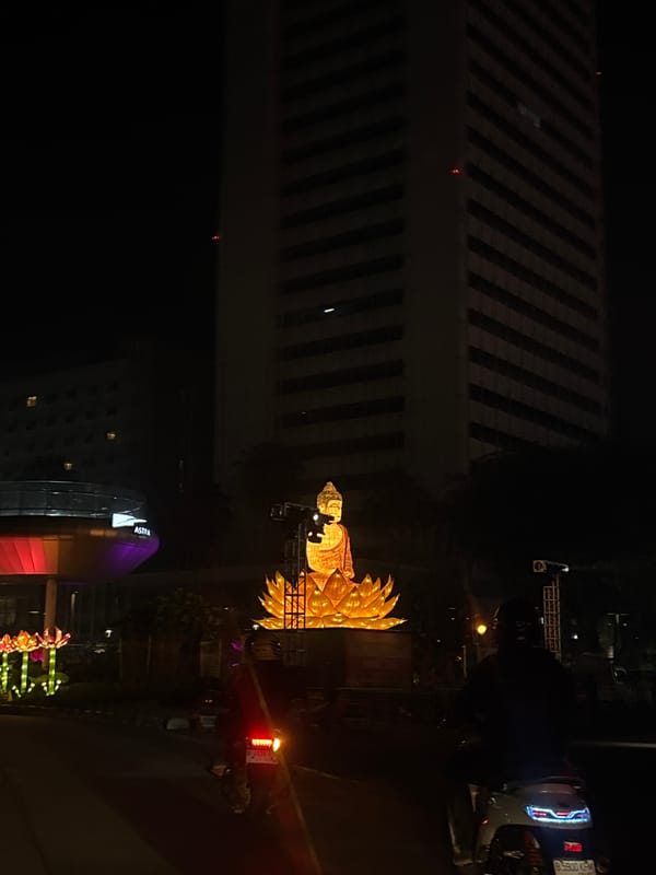 Motorcyclist passes illuminated Buddha statue in Central Jakarta night scene