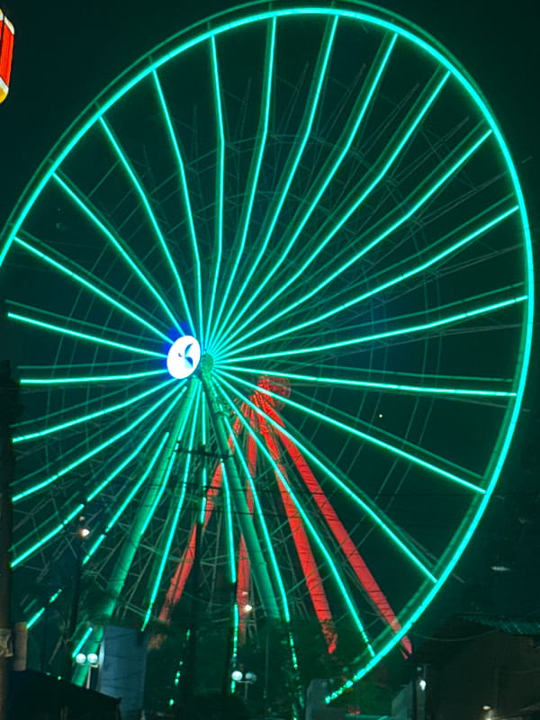 Green-lit Ferris wheel operates at night in Puebla