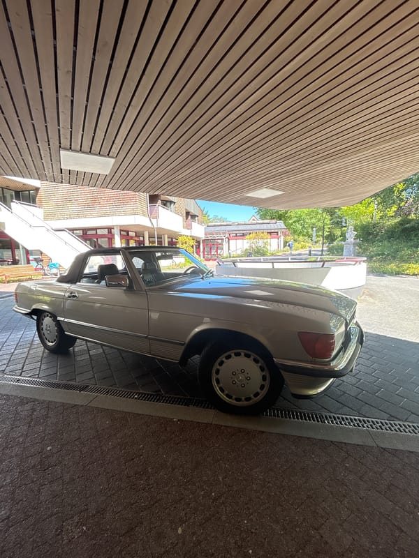 Vintage Mercedes R107 SL convertible parked under wooden overhang