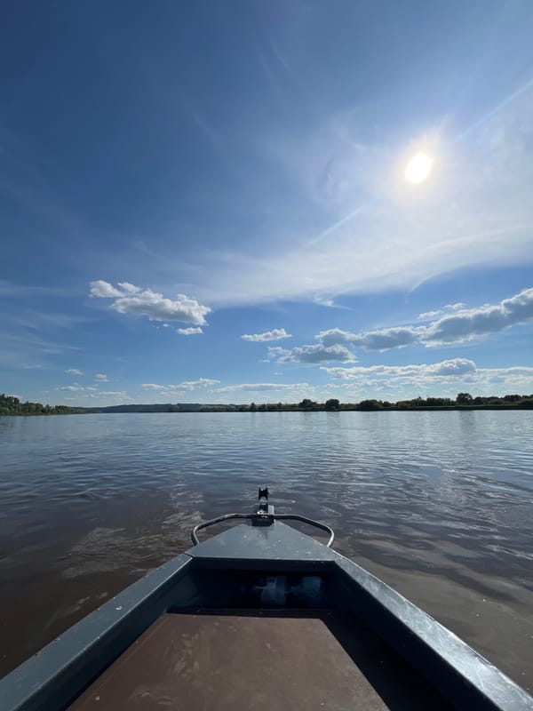 Motorboat cruising a calm, tree-lined river on a sunny day