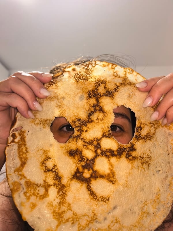 Person makes crepes, plays with pancake mask at unknown location