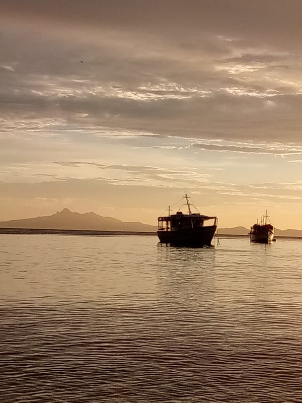 Two boats anchored at sunset beneath a cloudy mountain horizon