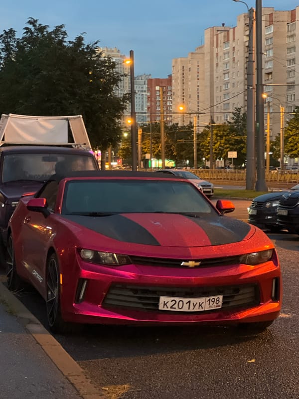 Red Camaro parked on a wet Saint Petersburg street at dusk