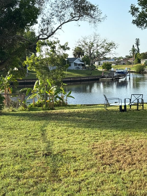 Waterside lawn seating setup with chairs and glass table