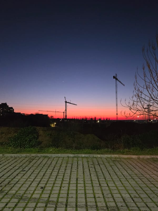 Construction cranes silhouetted against colorful evening sky in city