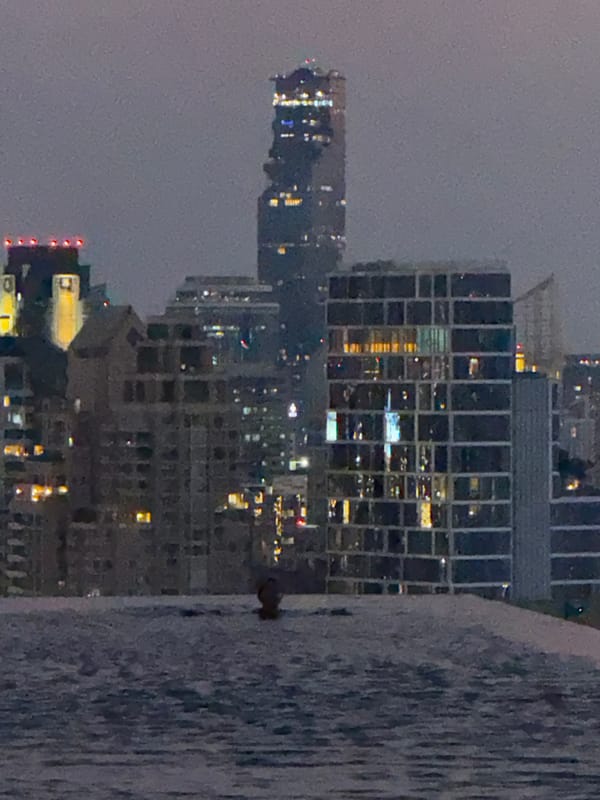 Person swims in Bangkok pool overlooking city skyline