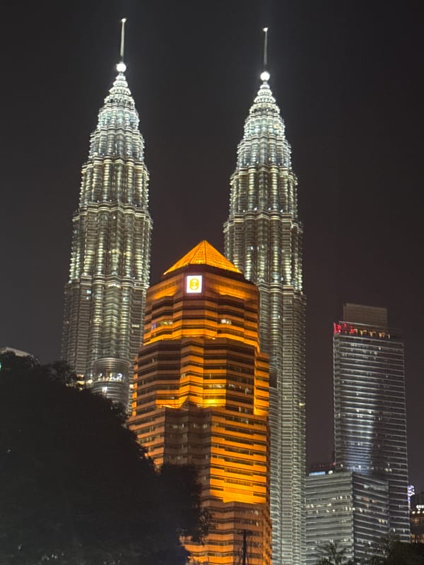 Tourists photograph illuminated Petronas Towers during evening visit