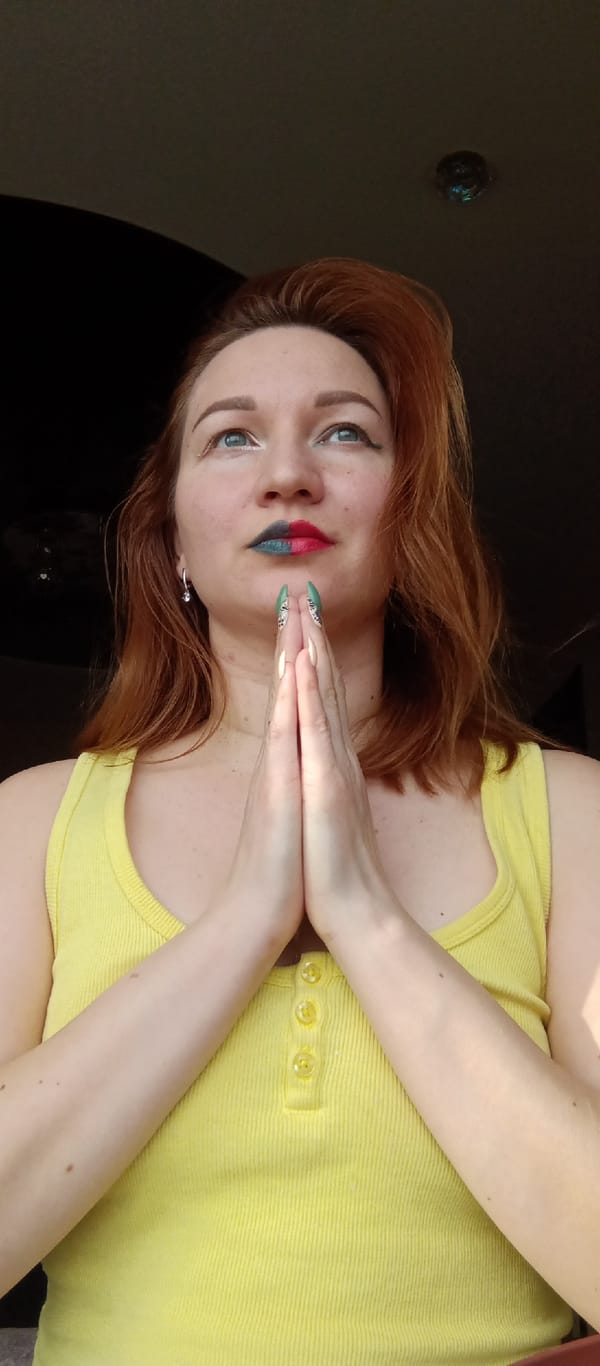 Red-haired woman in yellow tank top makes prayer gesture indoors
