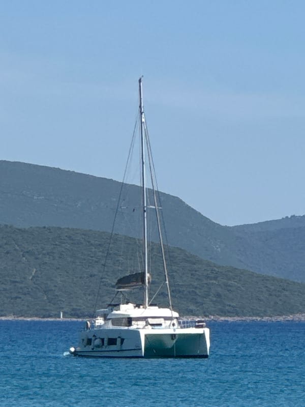 Lazy afternoon at a rocky cove with a catamaran anchored offshore