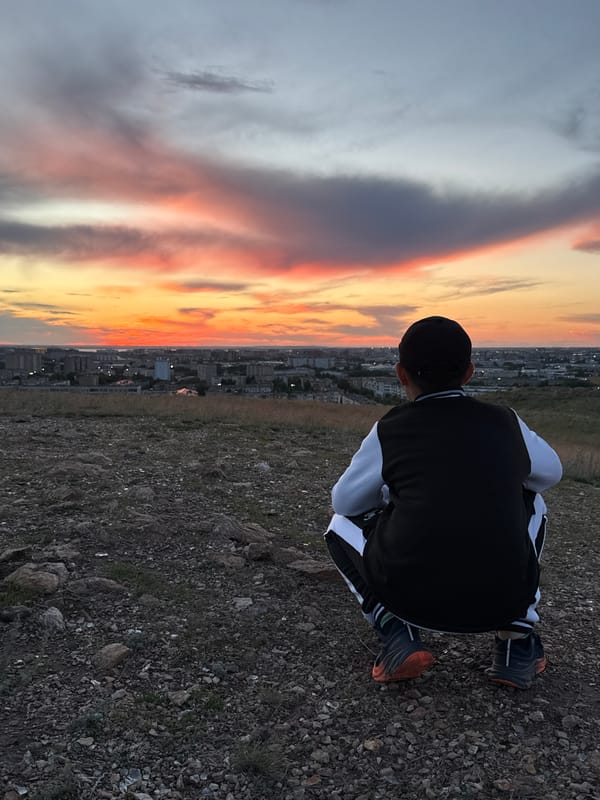 Young man watches sunset over Kokshetau from hillside overlook