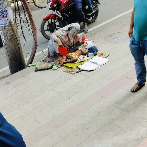 Woman fans child on sidewalk cloth near busy street