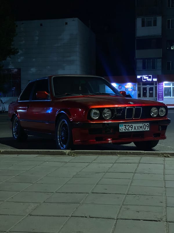 Red BMW E30 parked at night, headlights on